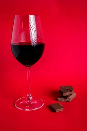 Glass of red wine with pieces of milk chokolate on red background. St. Valentines day concept. Copy space for your text.の写真素材