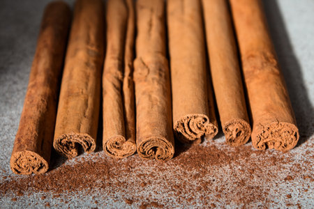 Ground Ceylon cinnamon sprinkled in front of real cinnamon sticks on a light background.の写真素材
