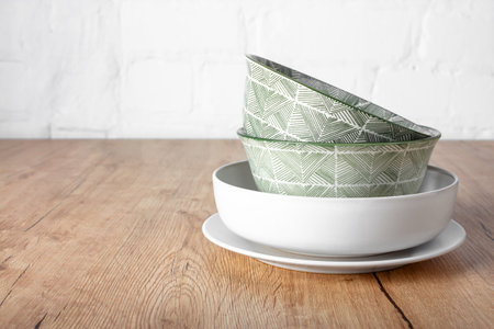 A set of clean dishes on a wooden table. Storing dishes in a stack. Inconvenient storage of dishes. A variety of bowls on a wooden table against a white brick wall.