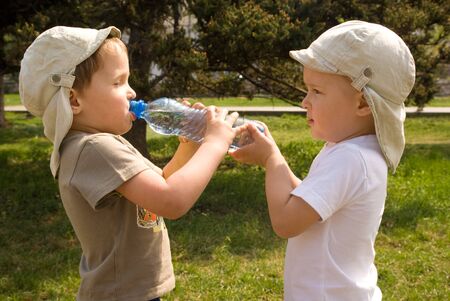 Two little boys drinking water from the bottle outdoorの写真素材
