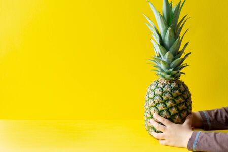 A delicious pineapple in a child's hand on a yellow backgroundの写真素材