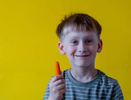 Boy eating fresh carrots on a yellow backgroundの写真素材