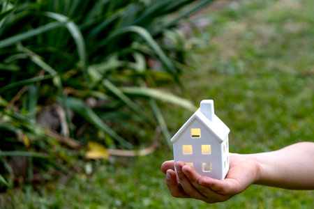 Childs hand holding small toy house on natural green blur background.の写真素材
