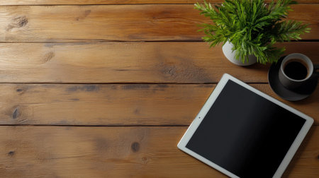 Flat lay of modern tablet with plant and mug on wood surface, minimalist workspace vibeの素材