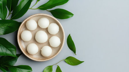 Top view of mochi treats arranged in a circle on a ceramic dish with leaves adding organic contrastの素材