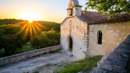 A stunning scene featuring a historic stone chapel bathed in warm sunlight during sunrise. The serene landscape highlights natural beauty with lush trees, creating a tranquil atmosphere for reflection.の素材