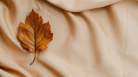 A vibrant autumn maple leaf rests gracefully on soft beige fabric, creating a serene still life composition that highlights nature's beauty and warmth.の素材
