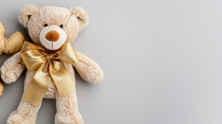 A charming teddy bear sits gracefully on a light gray surface, showcasing a golden bow, ideal for evoking warmth and affection in any space or gift.の素材