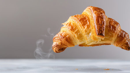 A beautifully crafted croissant hovers above a marble surface, exuding warmth and freshness. Light steam rises, enhancing its inviting aroma.の素材