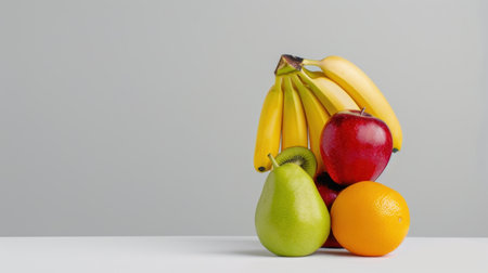 This image showcases a vibrant assortment of fresh fruits, including bananas, apples, a pear, a kiwi, and an orange, arranged stylishly against a neutral background.の素材