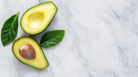 This image features fresh avocado halves showcasing vibrant green flesh and a visible seed, accompanied by green leaves, set against a stylish marble background.の素材