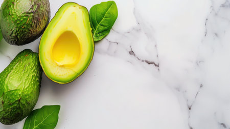 This image showcases fresh avocados arranged elegantly on a marble surface, highlighting their creamy pulp and lush green leaves, perfect for food-related content.の素材