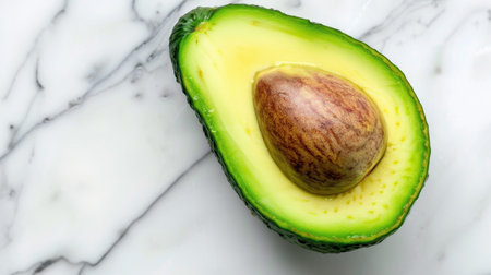 A fresh avocado halved with a prominent seed is beautifully displayed on a smooth marble surface, perfect for showcasing healthy eating and culinary creativity.の素材