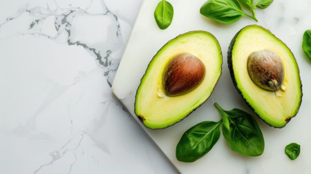 Freshly sliced avocado halves showcase their creamy texture, nestled on a white marble surface with vibrant basil leaves, perfect for healthy dishes.の素材