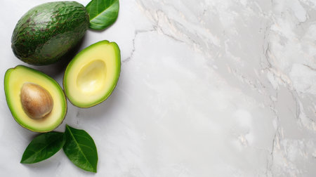 This image features fresh avocado halves beautifully arranged with green leaves on a stylish marble background, ideal for health and nutrition themes.の素材