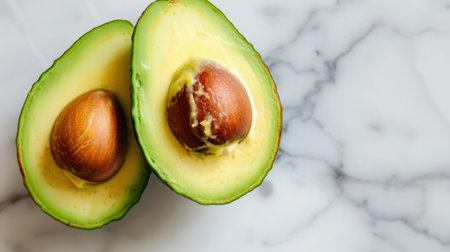 Freshly sliced avocado halves display creamy yellow flesh and a brown pit, set against an elegant marble background for a clean and vibrant look.の素材