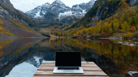 A serene scene featuring a sleek laptop on a wooden dock, set against the stunning backdrop of autumn foliage and majestic mountains reflecting in the calm lake.の素材
