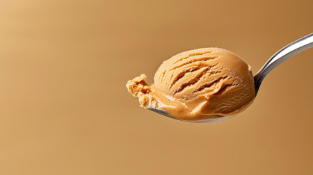 A mouthwatering scoop of peanut butter ice cream resting on a shiny spoon, highlighted against a smooth, warm backdrop, showcasing its rich, creamy texture.の素材