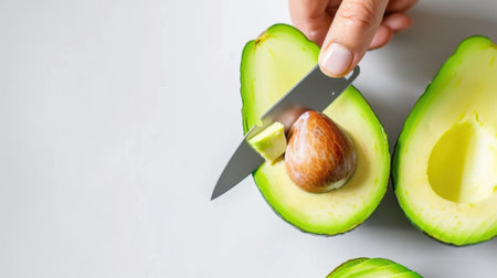 A close-up view of a fresh avocado being cut with a knife, showcasing its vibrant green flesh and large seed, perfect for healthy cooking and nutritious meals.の素材