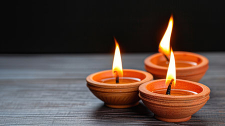 Three traditional oil lamps emit a gentle flame, creating a warm and inviting atmosphere against a dark background. Perfect for capturing serenity.の素材