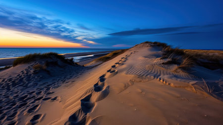 A serene view of sand dunes at sunset, with footprints leading towards the vast ocean. The peaceful coastal landscape evokes a sense of calm and adventure.の素材