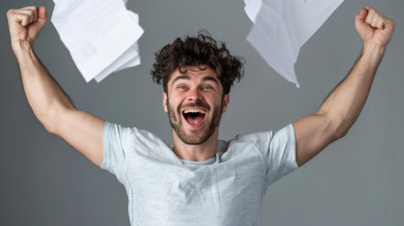 A joyful young man celebrates his success with raised arms and a wide smile while paper documents fly around him, capturing a moment of pure exhilaration.の素材