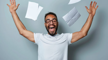 A joyful man celebrates by throwing papers in the air, conveying emotions of happiness and success, captured in a light gray studio background.の素材