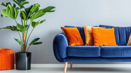 A stylish living room scene featuring a blue couch adorned with colorful pillows, a vibrant orange accent chair, and a lush green plant, creating a cozy atmosphere.の素材