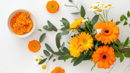 A stunning flat lay of vibrant orange and yellow flowers accompanied by greenery and a bowl of matching petals, perfect for spring and summerの素材