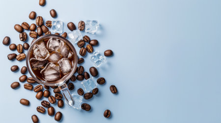 This image features a refreshing glass of iced coffee surrounded by coffee beans and ice cubes on a light blue background, perfect for summer vibes.の素材
