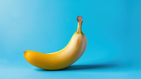 A vibrant yellow banana rests on a bright blue background, showcasing its freshness and nutritional benefits. Perfect for healthy eating themes.の素材