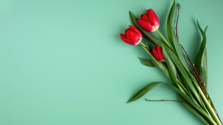 A stunning arrangement of fresh red tulips with lush green leaves on a soft green background, perfect for spring celebrations and floral decor.の素材