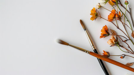This image features a serene artistic workspace showcasing paintbrushes and delicate orange flowers on a minimalist white background, perfect for inspiration and creativity.の素材