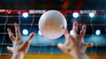 Captivating action shot of a volleyball in mid-air above reaching hands, with a net and bright gym lights in the background, capturing the essence of sports.の素材