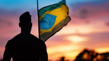 A captivating silhouette of a person proudly holding a Brazilian flag stands against a stunning sunset. The sky is filled with colorful clouds, capturing a moment of pride and tranquility in nature.の素材
