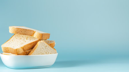 A stack of fresh white bread slices placed in a bowl against a soft blue background, perfect for illustrating culinary themes and food presentations.の素材