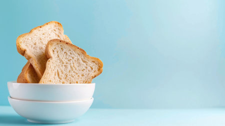 Delight in the simplicity of freshly toasted bread slices arranged in a stylish white bowl on a soft blue background, perfect for breakfast inspiration.の素材
