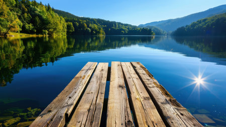 A picturesque wooden dock extends over a tranquil lake, offering captivating reflections of lush greenery and majestic mountains under a clear blue sky.の素材