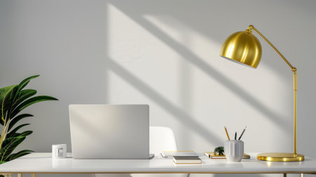 A stylish modern office workspace featuring a sleek laptop, a golden desk lamp, and a lush green plant, illuminated by soft sunlight and shadows.の素材