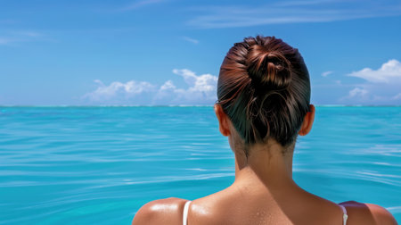 A serene woman gazes over the tranquil turquoise water, immersed in the beauty of a bright blue sky dotted with fluffy clouds, inviting relaxation and escape.の素材