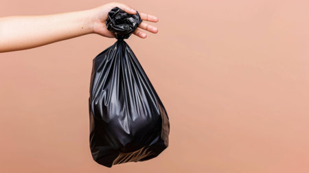 A person holds a black plastic trash bag tightly in one hand, emphasizing the importance of waste disposal and cleanliness in daily life.の素材