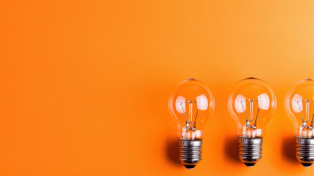 This image features three vintage light bulbs against a vibrant orange background, symbolizing creativity and innovation in design. Perfect for various artistic and commercial uses.の素材