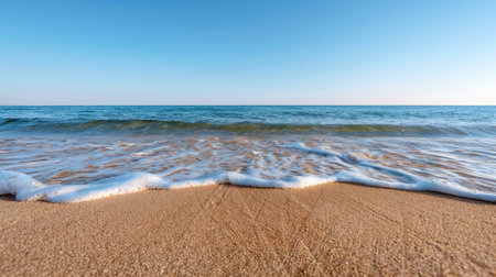 A picturesque view of tranquil ocean waves gently lapping against a golden sandy beach under a clear blue sky, evoking feelings of peace and relaxation.の素材
