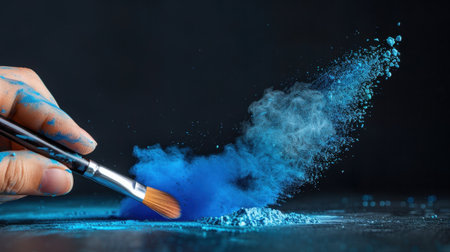 A captivating image showcasing a hand using a brush to create a vibrant blue powder cloud against a dark background, symbolizing artistic creativity.の素材