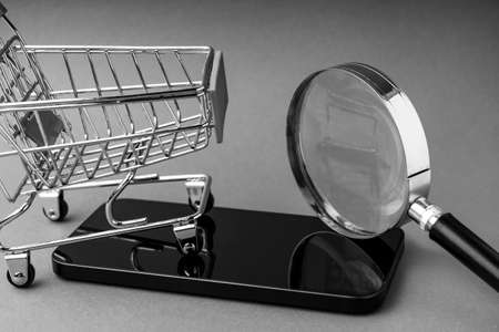 An empty shopping cart and a modern smartphone on a red scarlet background.