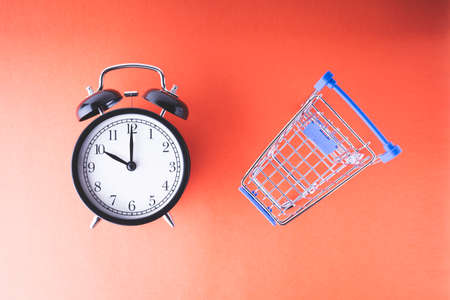 An empty shopping cart and an alarm clock on a red scarlet backgroundの写真素材