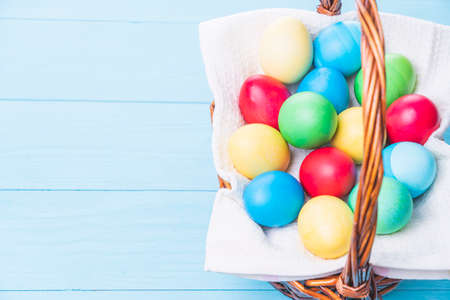 basket with colorful Easter eggs on a blue wooden backgroundの写真素材