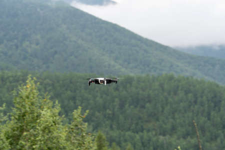 A modern drone flies in the mountains. quadcopter on the background of a mountain landscape, Altai,...