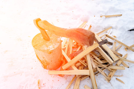 an ax and firewood in the snow, a finely chopped wooden log for heating the house in the absence of gas heating, solar glare, selective focus. High quality photoの写真素材