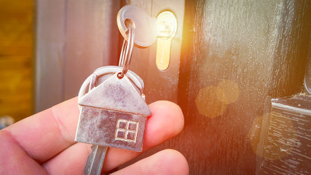 the key in the lock of the front door and a keychain in the form of a house close-up, solar glare, selective focusing, tinted image, the concept of buying and renting real estate, a mortgage symbolの写真素材